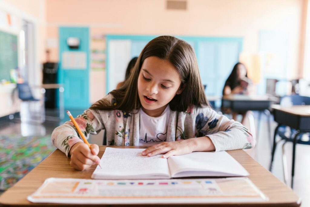 Focused young girl writing in her notebook in a classroom setting, showcasing learning and education.