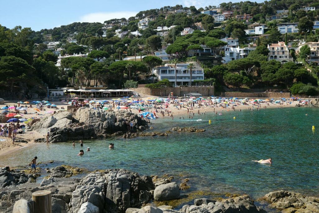 Crowded summer beach scene with turquoise waters and houses on Costa Brava.