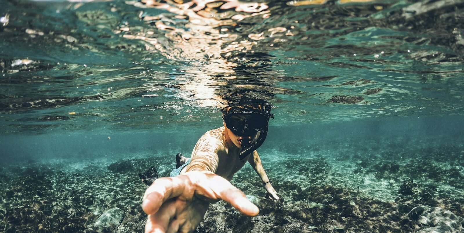 underwater photography of man wearing snorkel lending his hand