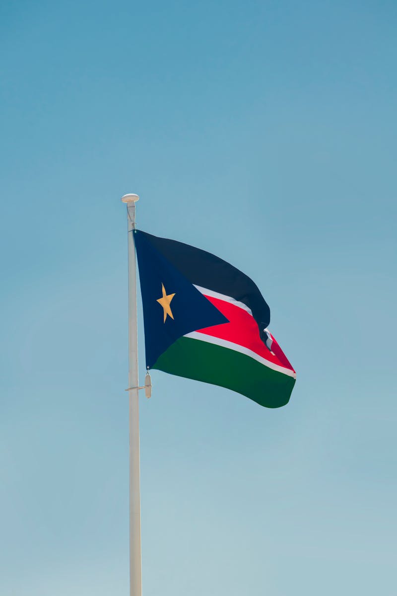South Sudan national flag fluttering on a flagpole under a clear blue sky, symbolizing patriotism.