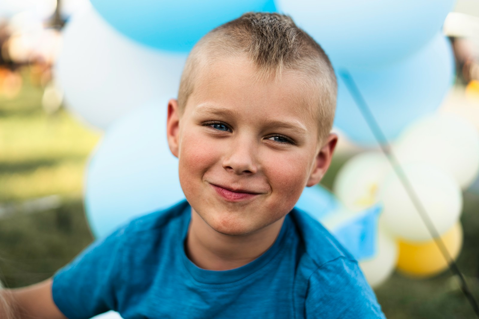 a young boy smiles at the camera with balloons in the background