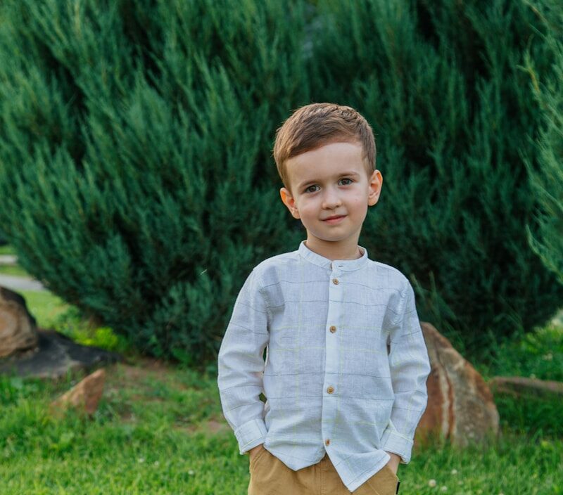 boy in blue dress shirt and brown pants standing on green grass field during daytime