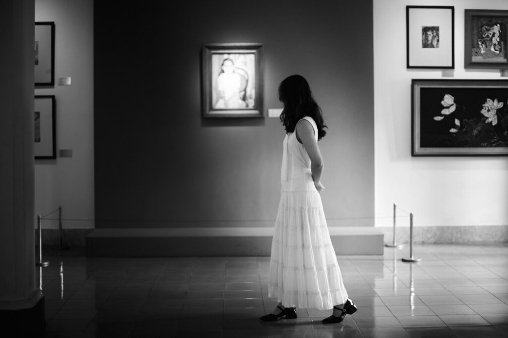 Woman in white dress observes art in gallery