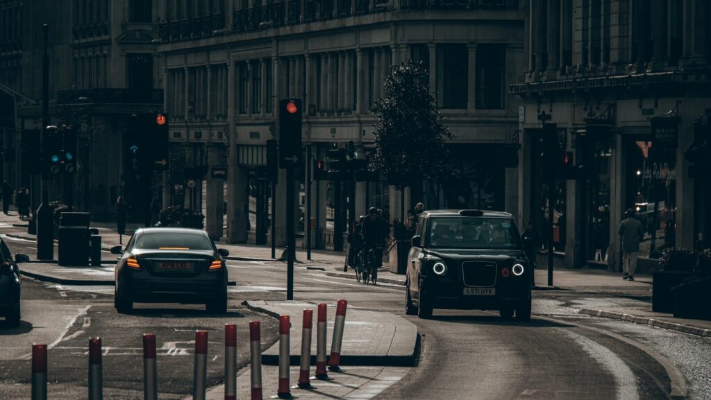 Black london taxi and car driving on city street.
