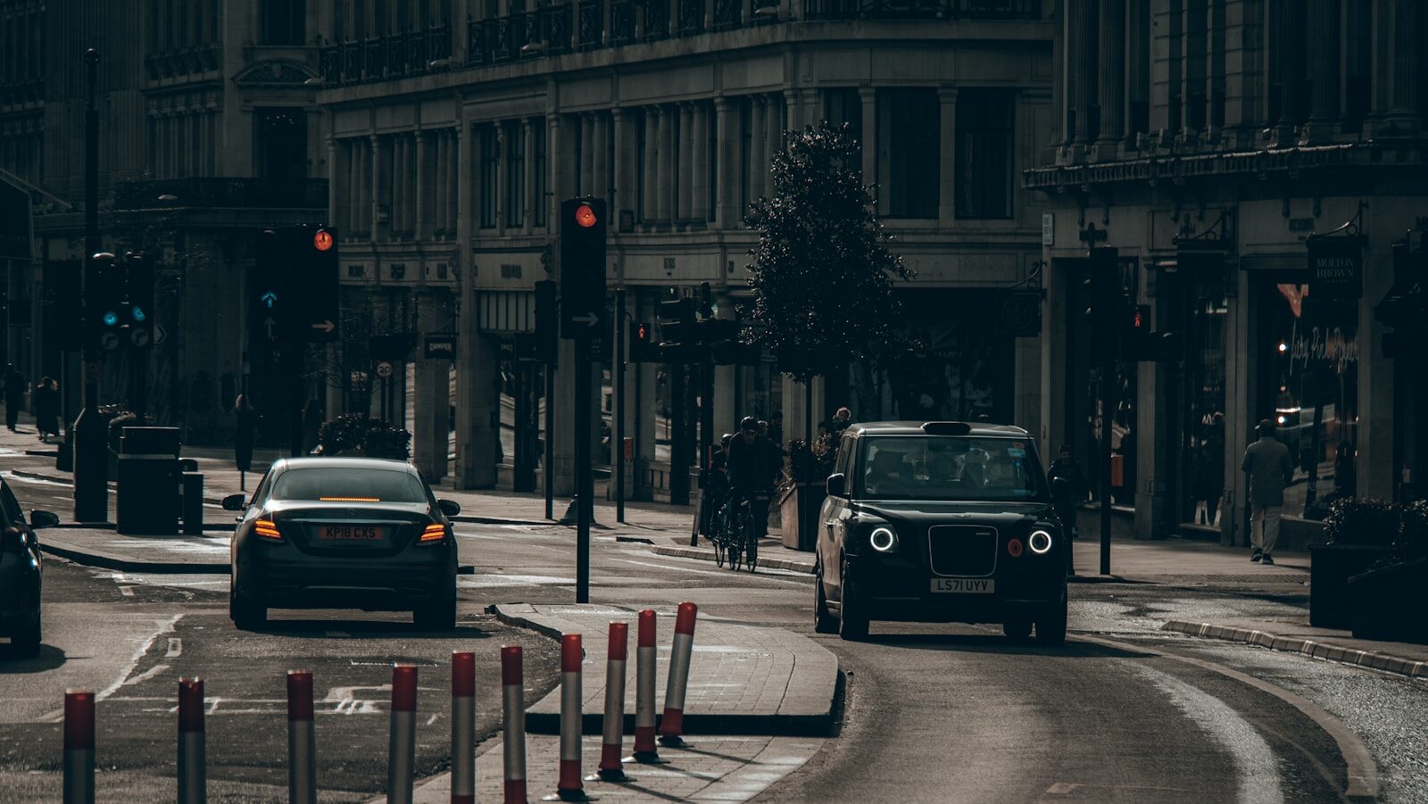 Black london taxi and car driving on city street.