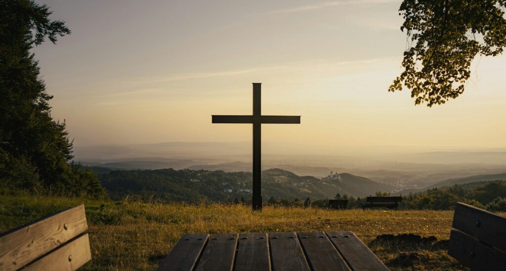 A cross stands on a hill overlooking the scenery.