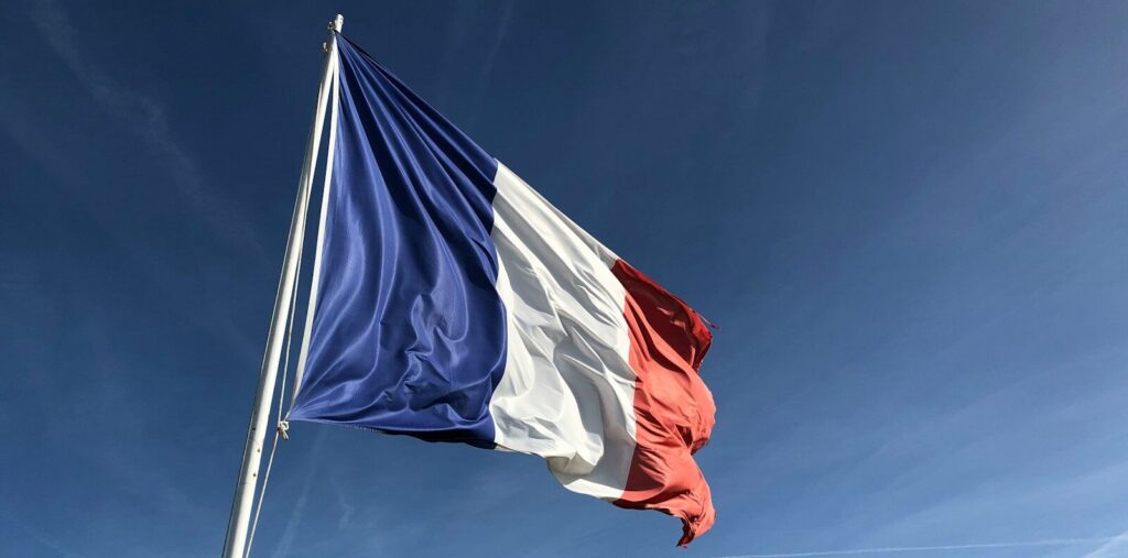 The French flag waving on a flagpole against a clear blue sky